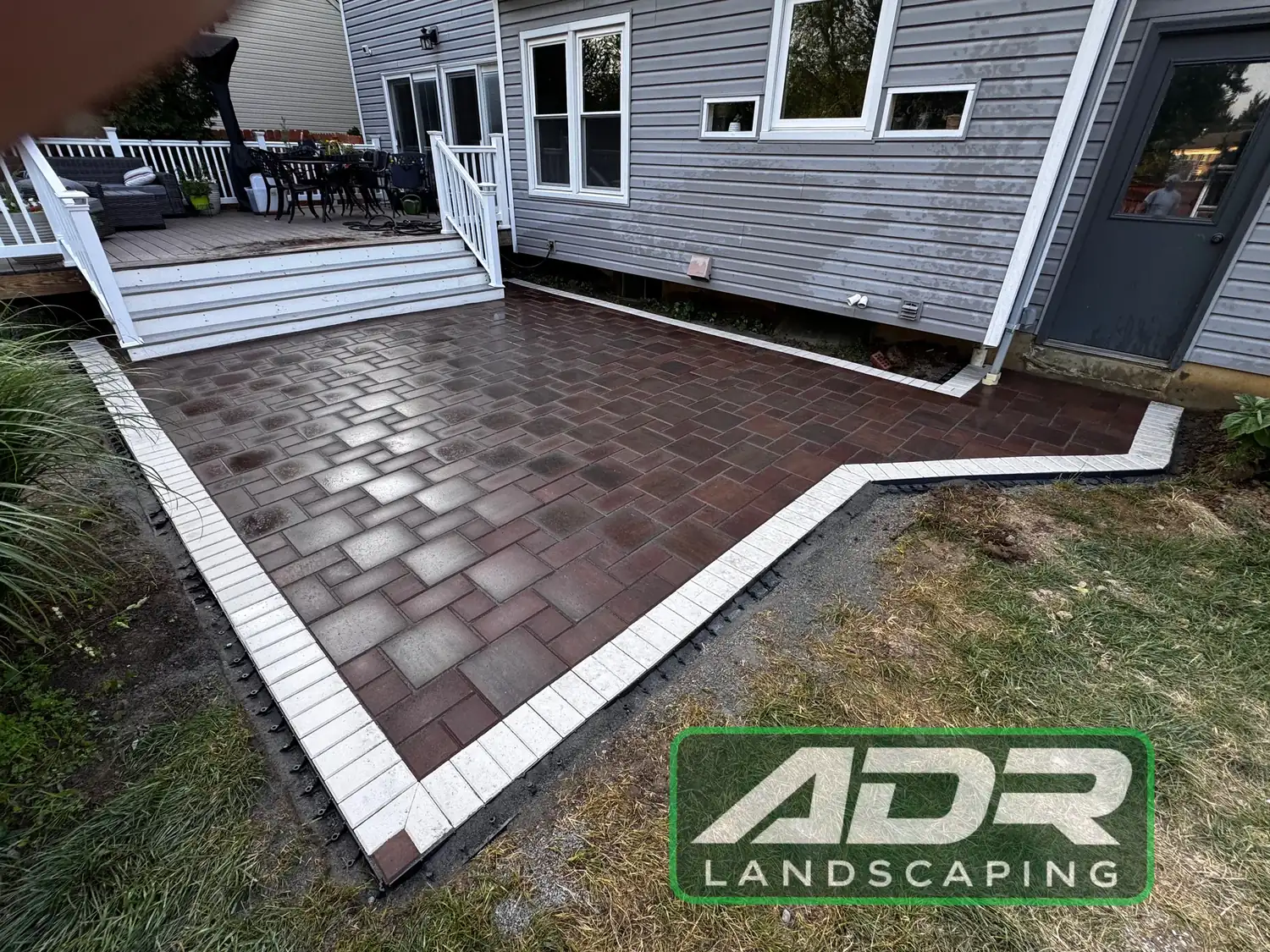Red and charcoal paver patio with a white border course beside a deck
