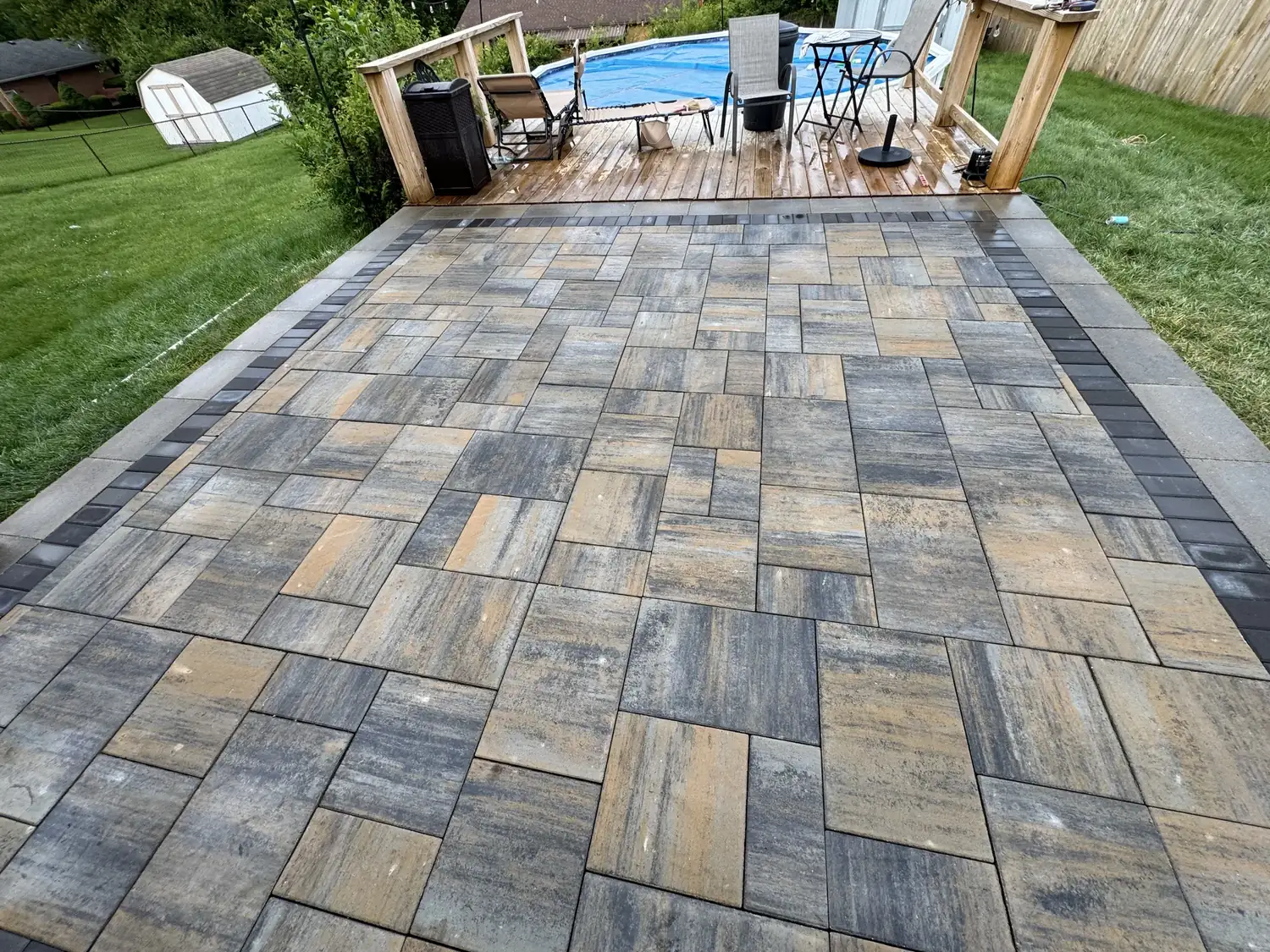 Large multi size paver patio with a dark soldier course border running up to a deck