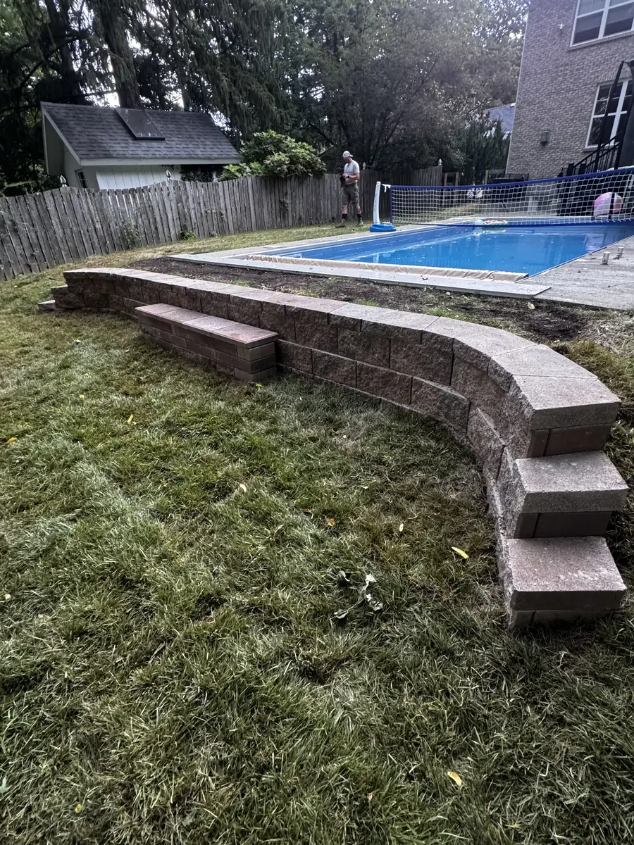 Curved block retaining wall with an integrated bench installed beside an in ground pool